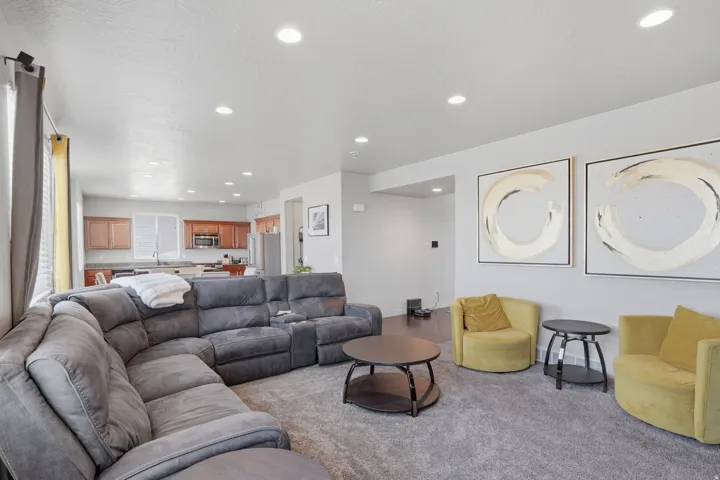 Open-concept living area with recessed lighting, light gray wall tones, gray carpeting, and a visible kitchen