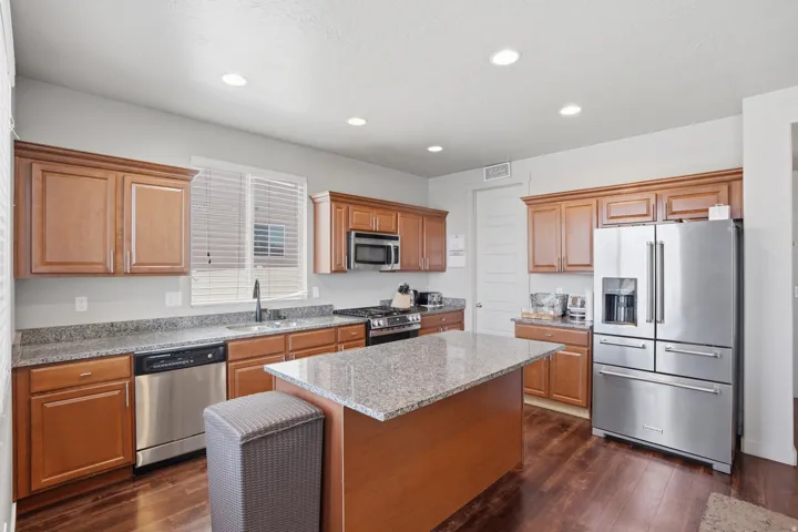 Kitchen featuring wood-finish cabinetry, granite-style countertops, stainless steel appliances, a center island with additional counter space, and wood-finish flooring