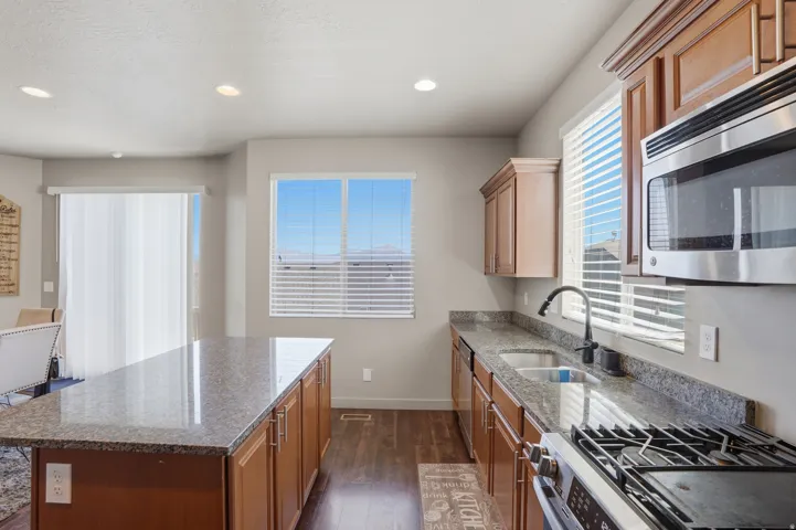 Kitchen featuring a central island with a stone-finish countertop, wood cabinetry, stainless steel appliances, and wood-finish flooring
