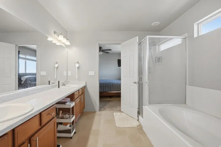 Bathroom featuring a dual vanity with wood cabinetry, a full-width mirror, a separate glass-enclosed shower, and a built-in bathtub