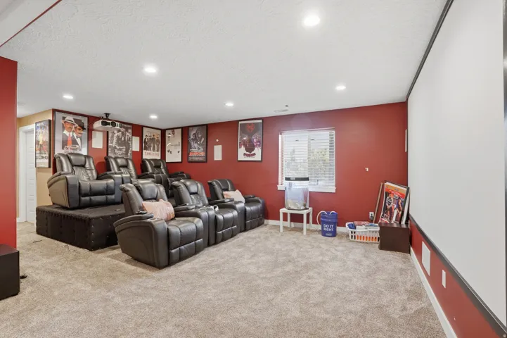 Theater room with tiered seating, wall-mounted screen, and recessed lighting