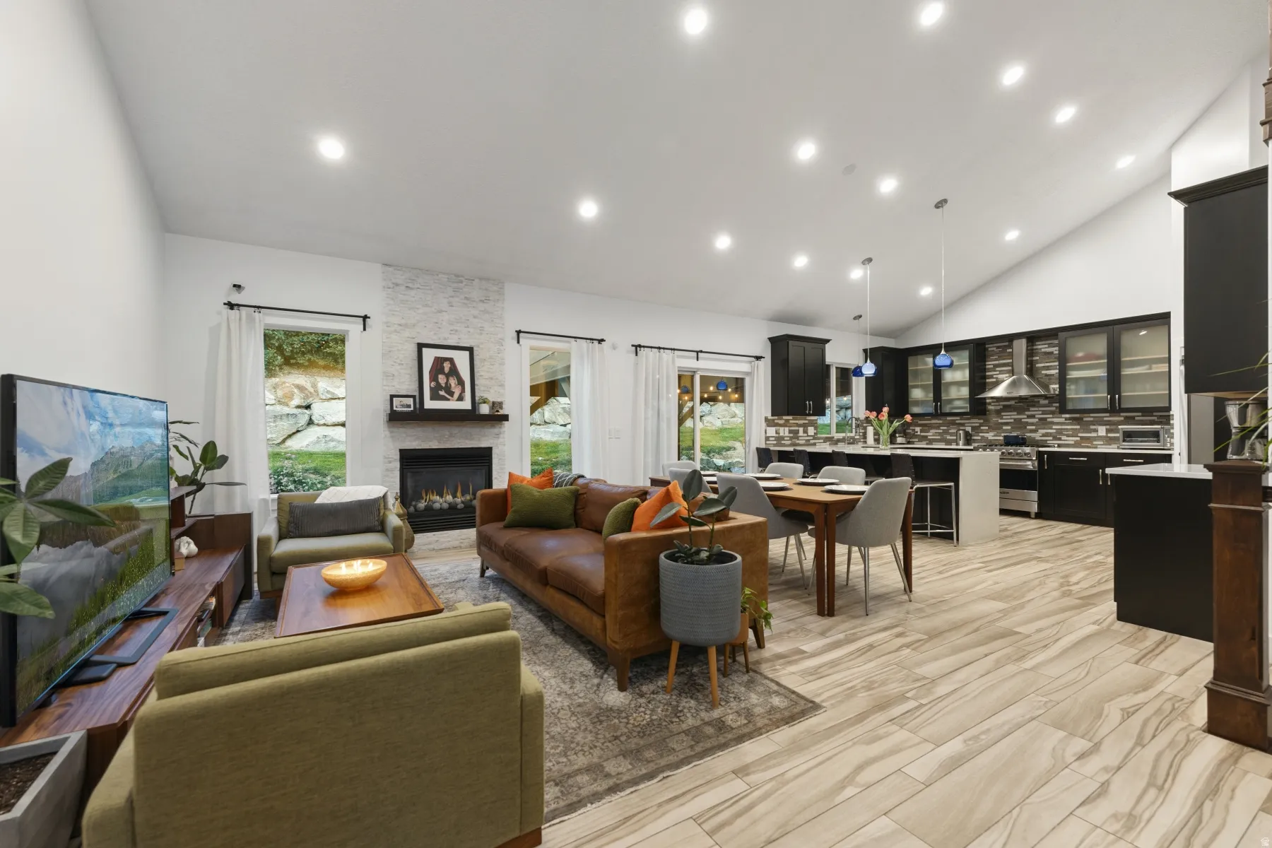 Living area with lofted ceiling, recessed lighting, a stone fireplace, and light wood finished floors