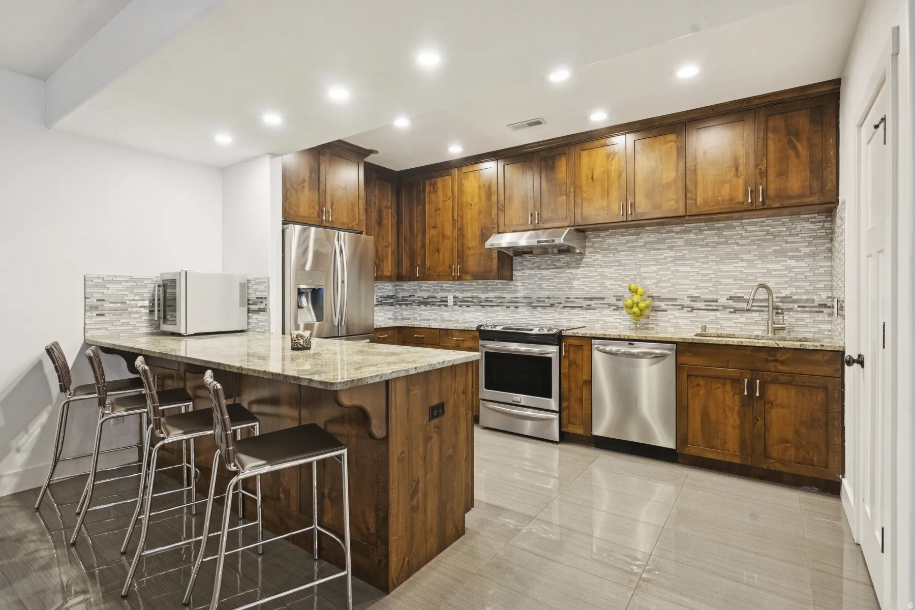 Kitchen with light stone counters, a breakfast bar area, a peninsula, stainless steel appliances, and recessed lighting