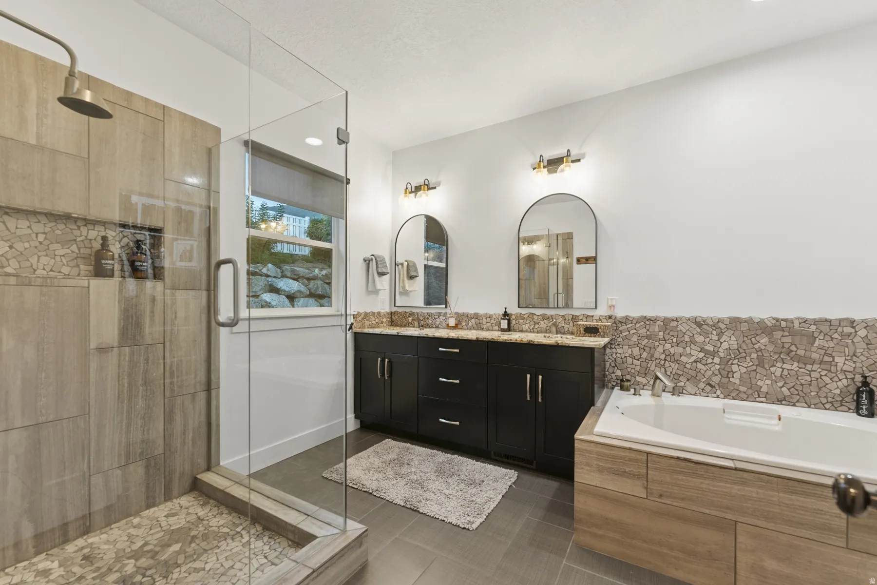 Bathroom with double vanity, a garden tub, a shower stall, and dark tile patterned flooring