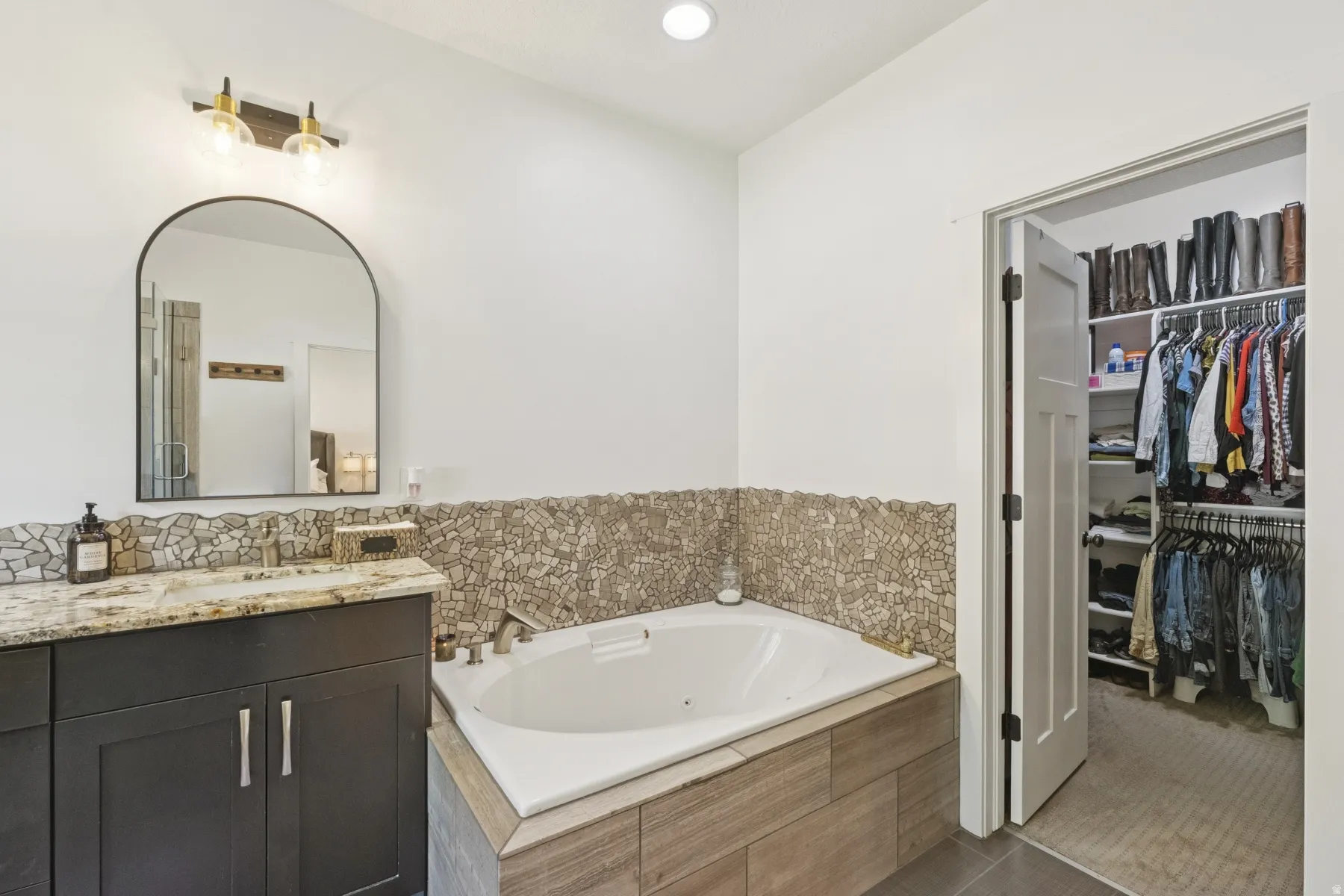 Bathroom with a tub with jets, vanity, a walk in closet, recessed lighting, and tile patterned floors