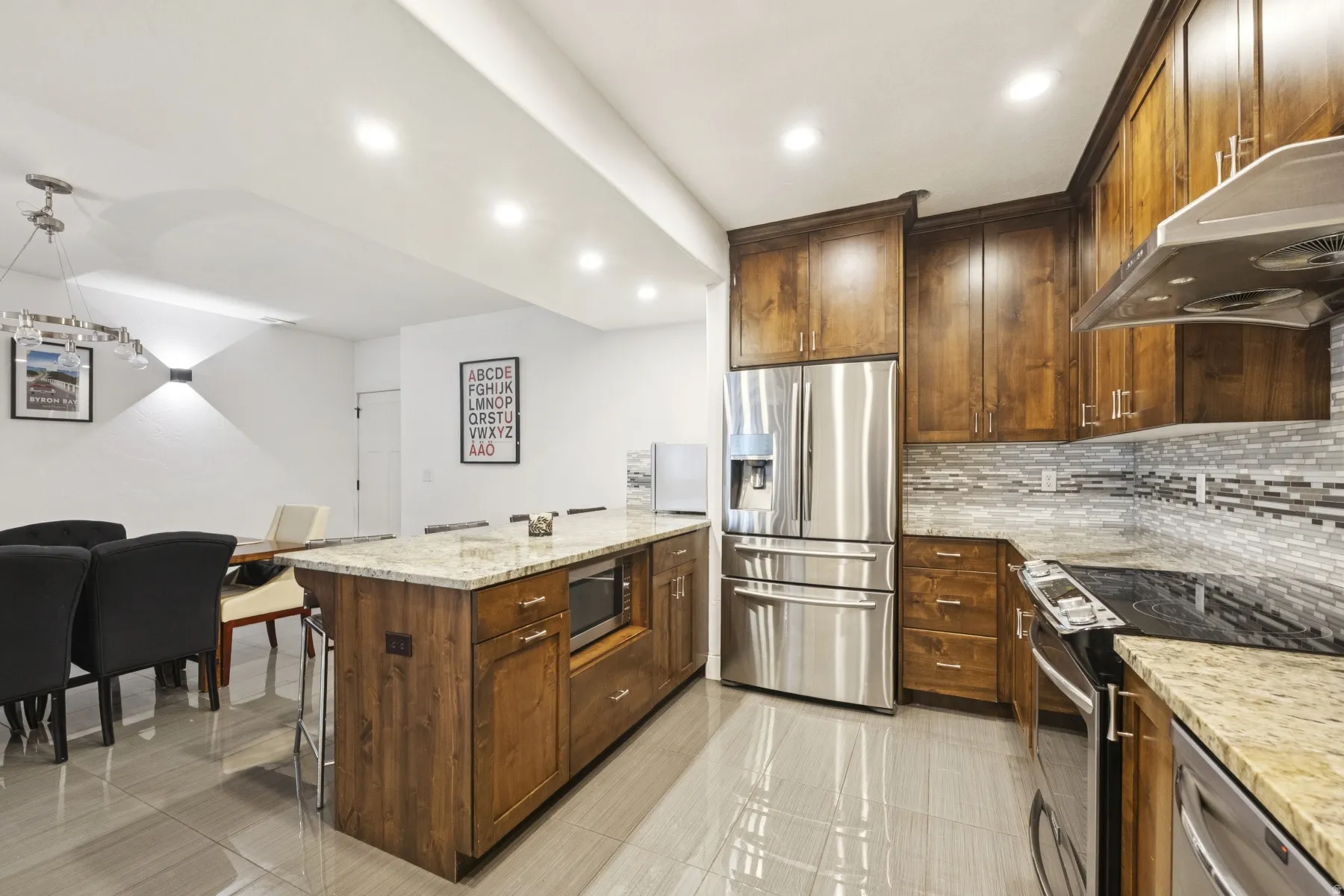 Kitchen featuring stainless steel appliances, a peninsula, light stone counters, backsplash, and decorative light fixtures
