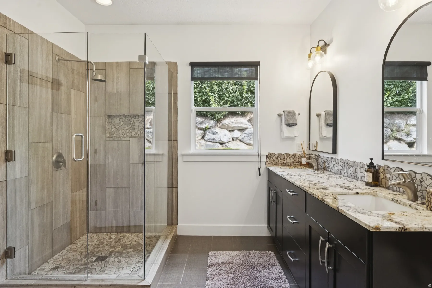 Bathroom featuring double vanity, a shower stall, and dark tile patterned floors