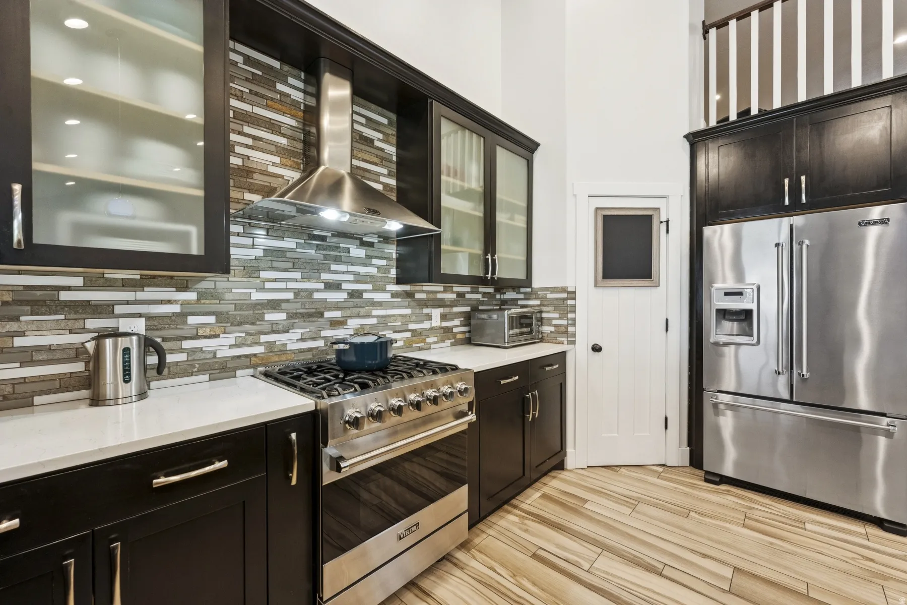 Kitchen with glass insert cabinets, high quality appliances, light stone counters, light wood-style flooring, and decorative backsplash