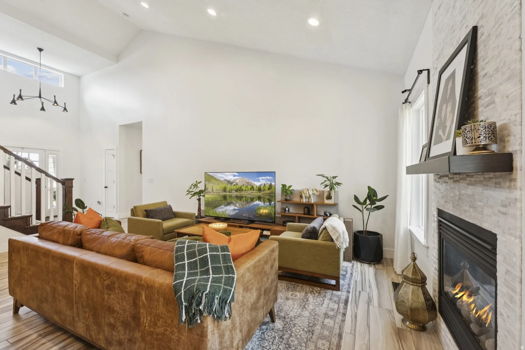 Living room with a large fireplace, light wood-type flooring, vaulted ceiling, recessed lighting, and plenty of natural light