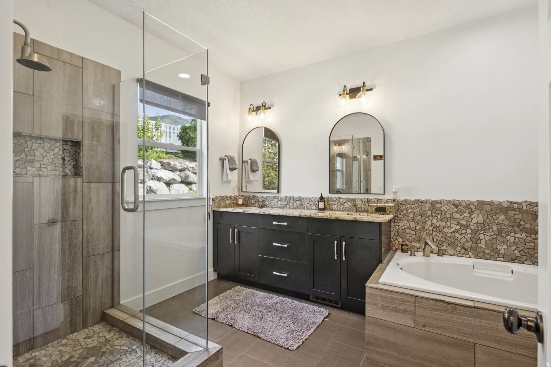 Full bathroom featuring double vanity, a bath, a shower stall, and dark tile patterned floors
