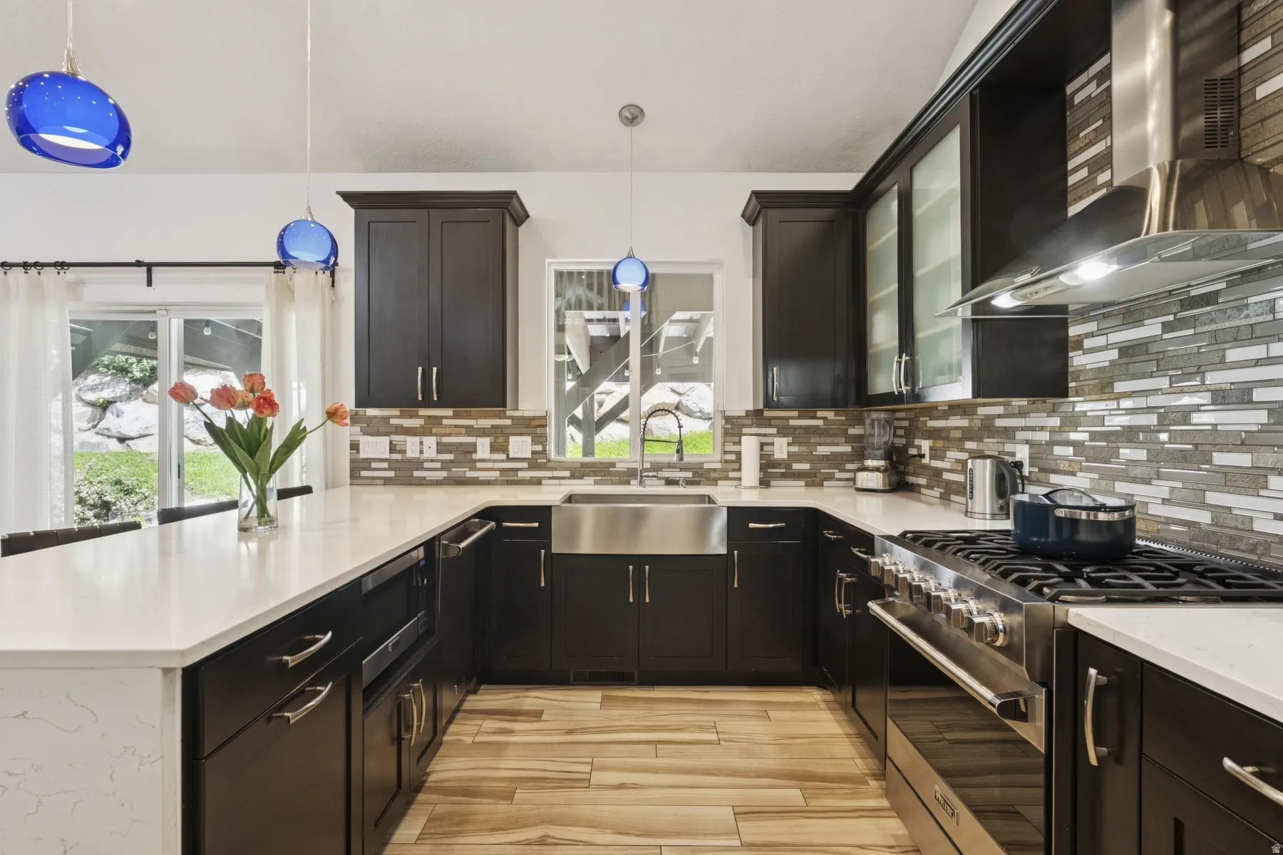 Kitchen with a peninsula, stainless steel gas range, decorative backsplash, light stone countertops, and light wood finished floors