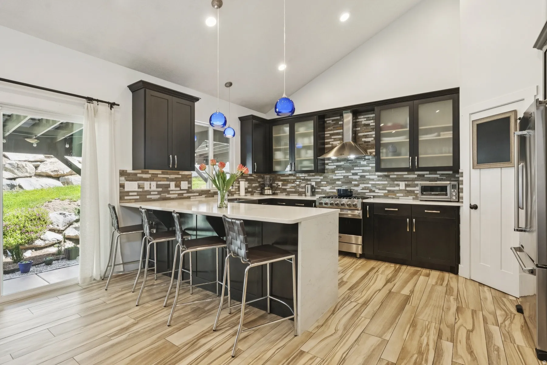 Kitchen featuring vaulted ceiling, decorative light fixtures, a peninsula, a breakfast bar area, and light wood-type flooring