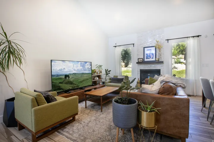 Spacious living area featuring a vaulted ceiling, wood-finish flooring, and a fireplace with a stacked stone facade and dark wood mantel