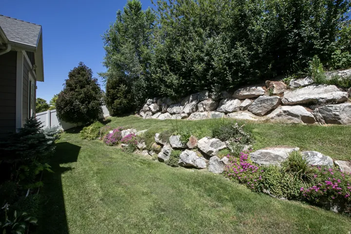Tiered landscaping featuring a rock retaining wall, mature trees, and vibrant groundcover