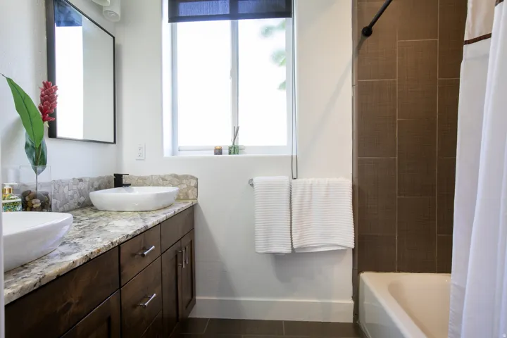 Bathroom featuring dual vessel sinks set on a granite-topped vanity with dark wood-finish cabinetry
