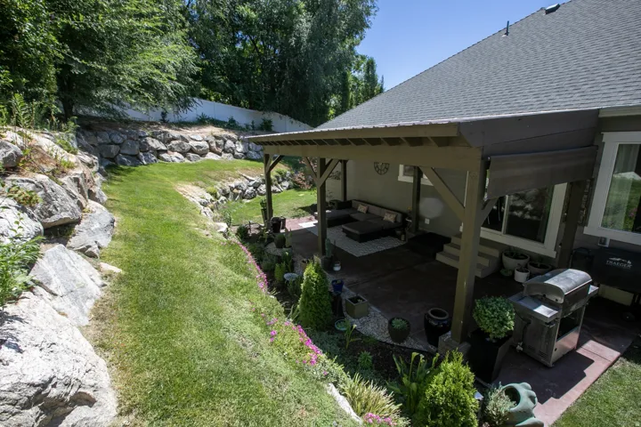 Expansive terraced backyard featuring natural rock retaining walls, a manicured lawn, and a covered patio with a wood-frame pergola