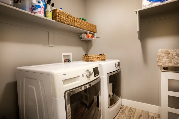 Dedicated laundry area featuring wood-finish flooring, light neutral wall paint, white baseboards, and built-in shelving for storage