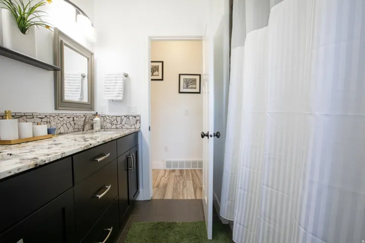 Bathroom vanity featuring dark wood cabinetry with brushed nickel hardware, a speckled countertop, and a mosaic tile backsplash