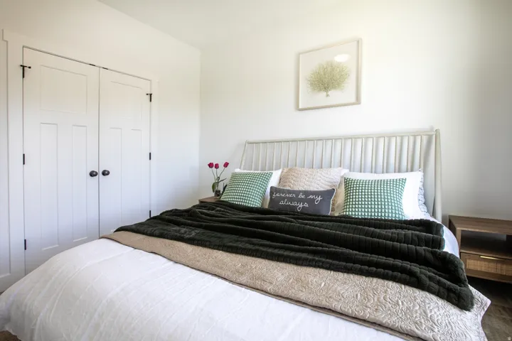 White paneled closet doors with dark hardware, a light-toned headboard, and a wood-finish side table