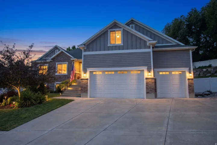 Exterior featuring stone and siding finishes, a concrete driveway, dual garage doors with integrated windows, a stepped entryway, and landscape lighting
