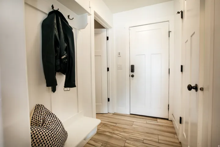 Entryway featuring light wood-finish flooring, white panel doors with black hardware, and a built-in bench with wall hooks