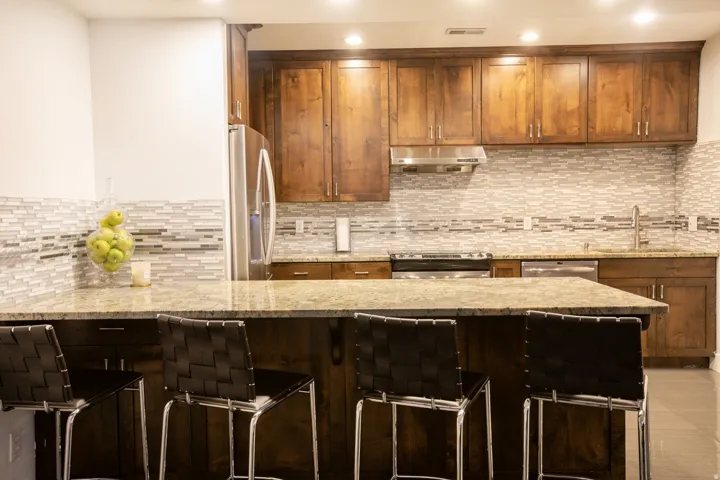 Kitchen featuring an island with stone countertop, stainless steel appliances, wood cabinetry, and a mosaic tile backsplash
