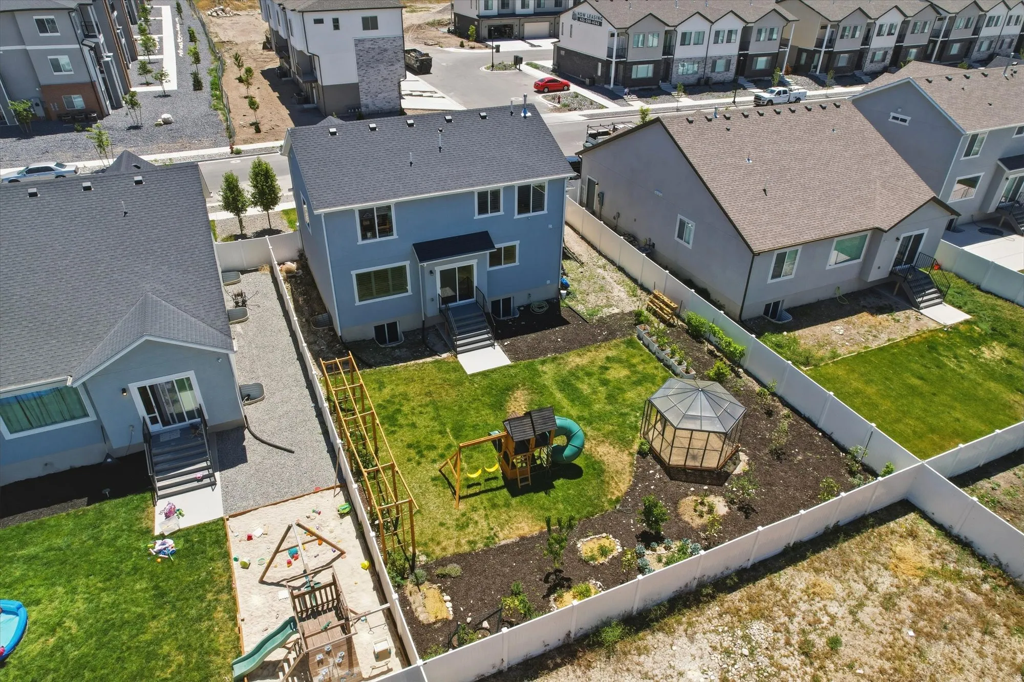 Expansive backyard featuring a manicured lawn, a white privacy fence, and a dedicated garden area with a greenhouse structure