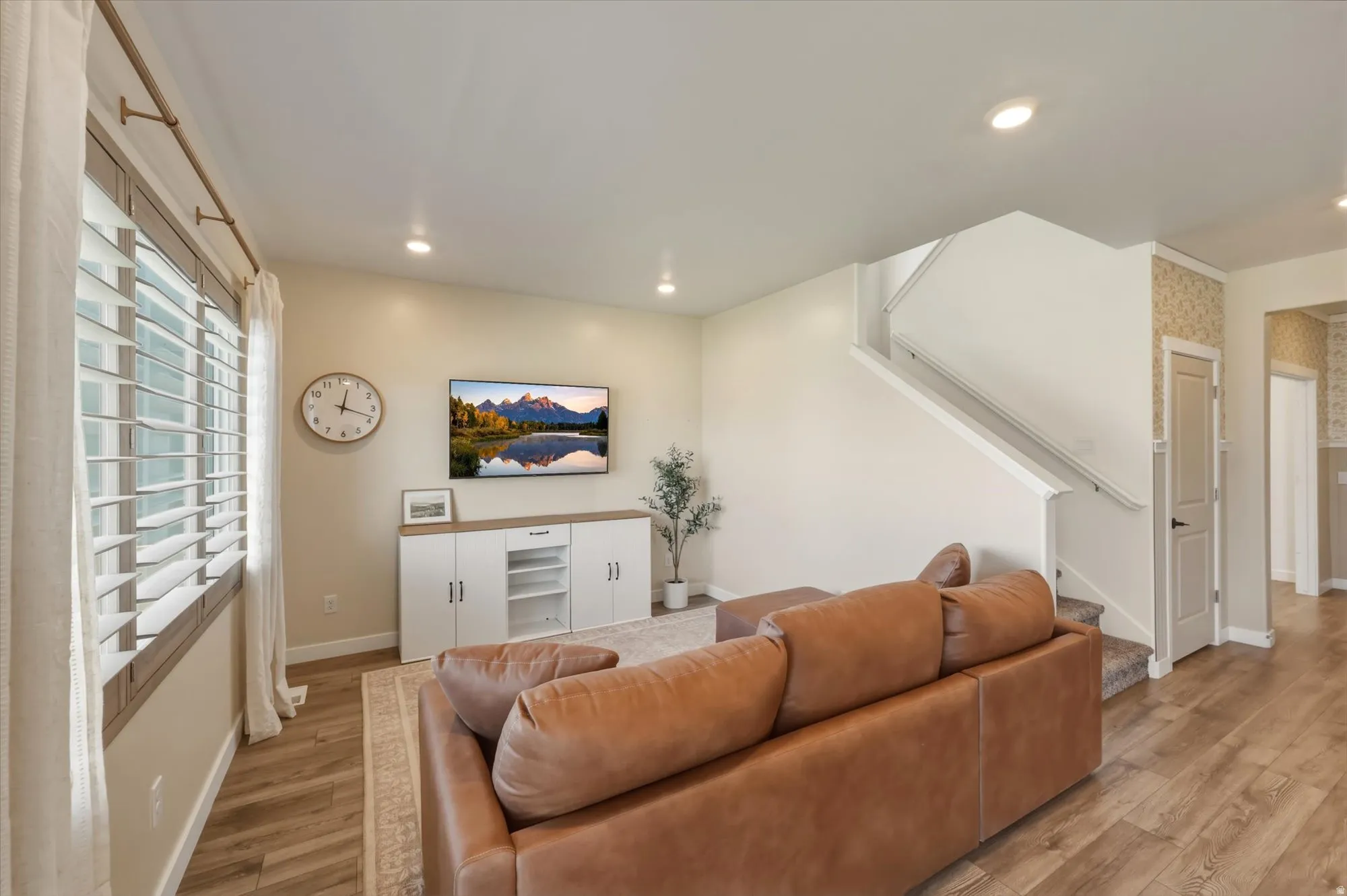 Living area featuring wood-finish flooring, recessed lighting, white window shutters, a staircase with white balusters, and a built-in media console with white cabinetry
