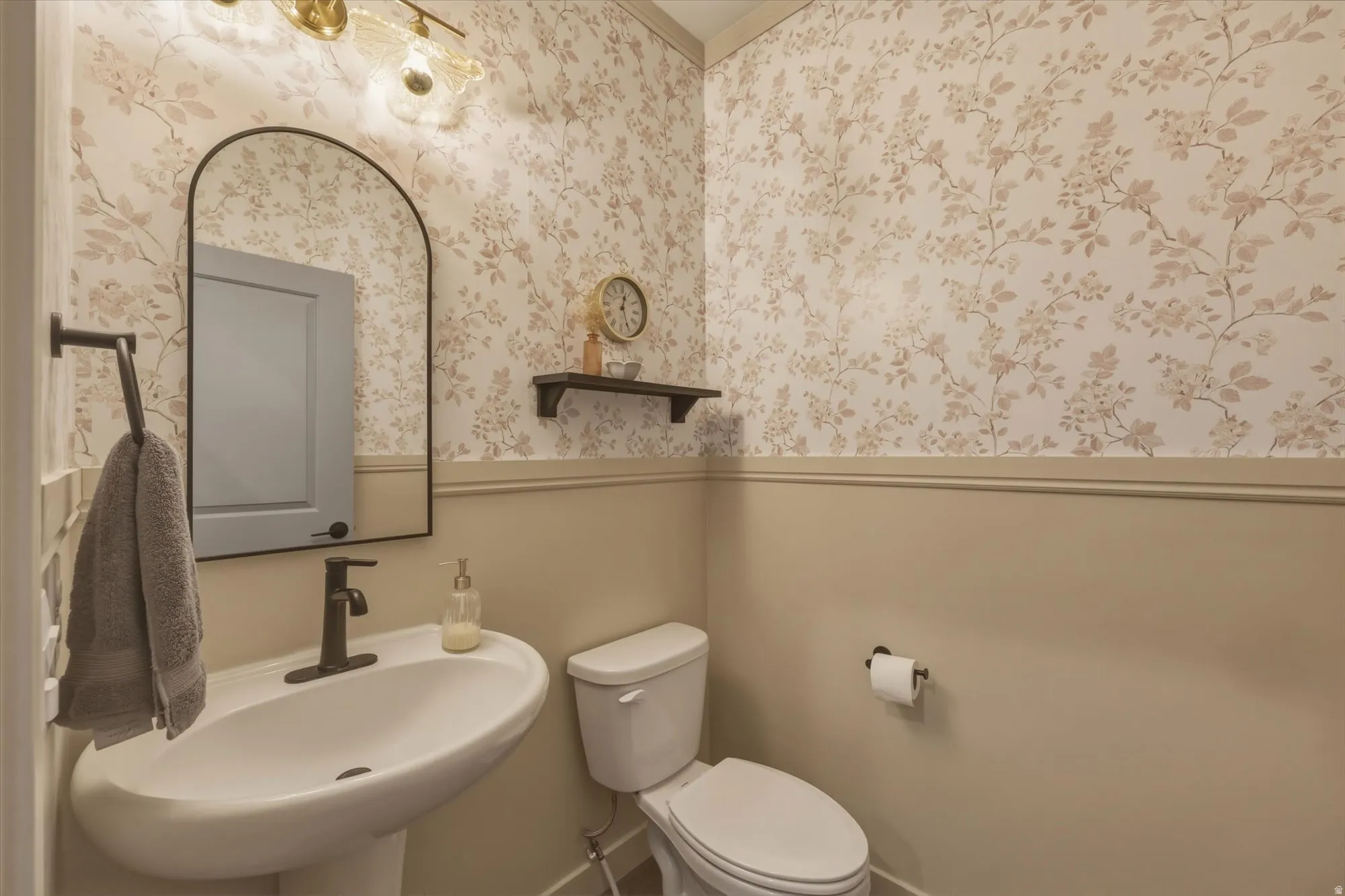 Pedestal sink with a matte black faucet, complemented by a black-framed arched mirror