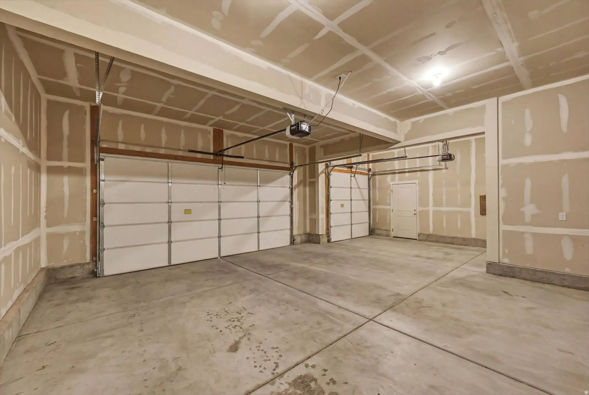 Spacious garage featuring a concrete floor, three panel-style garage doors, two garage door openers, and an interior access door