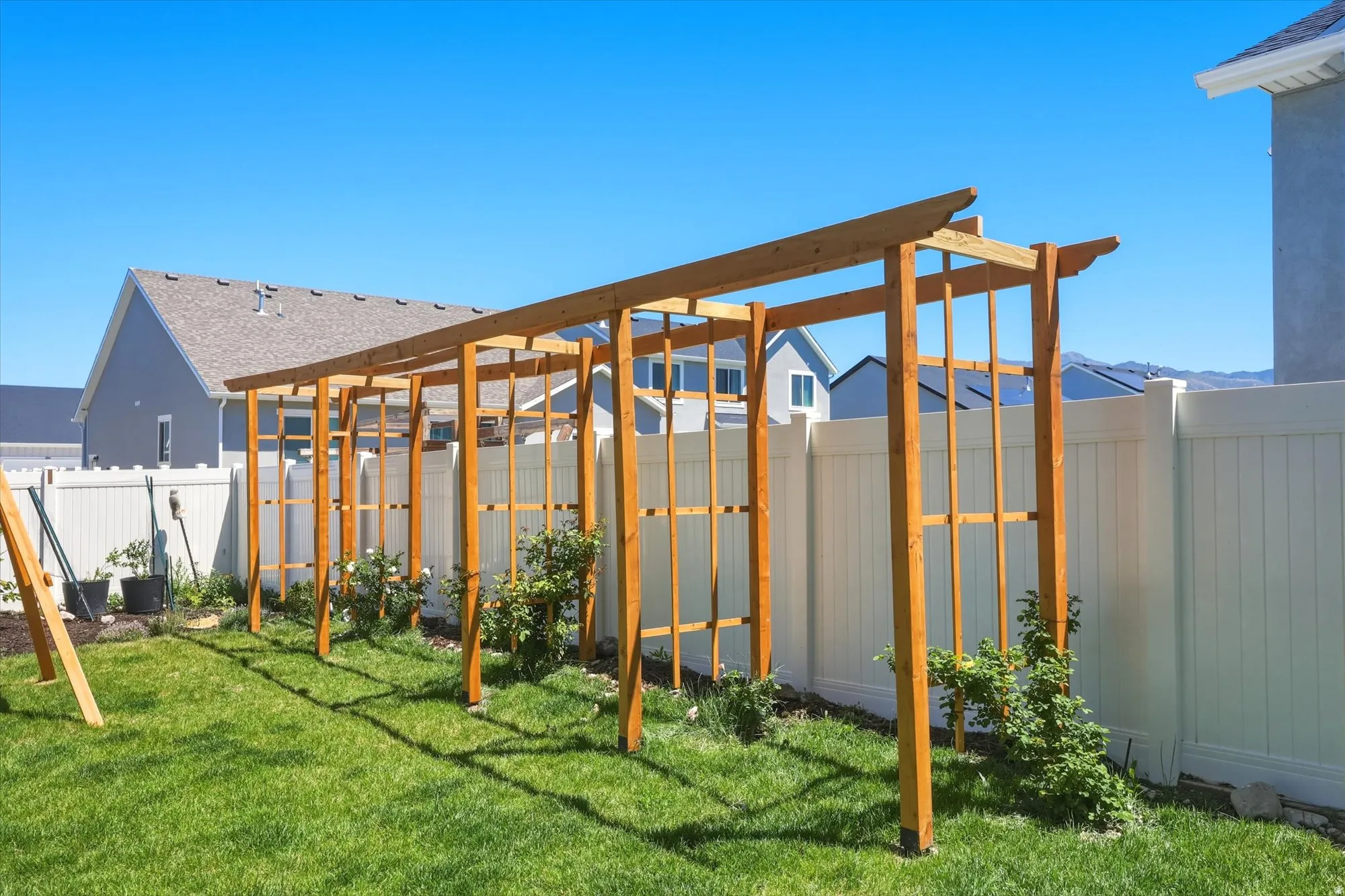 Expansive backyard featuring a wood trellis structure, manicured lawn, white privacy fencing, and garden beds
