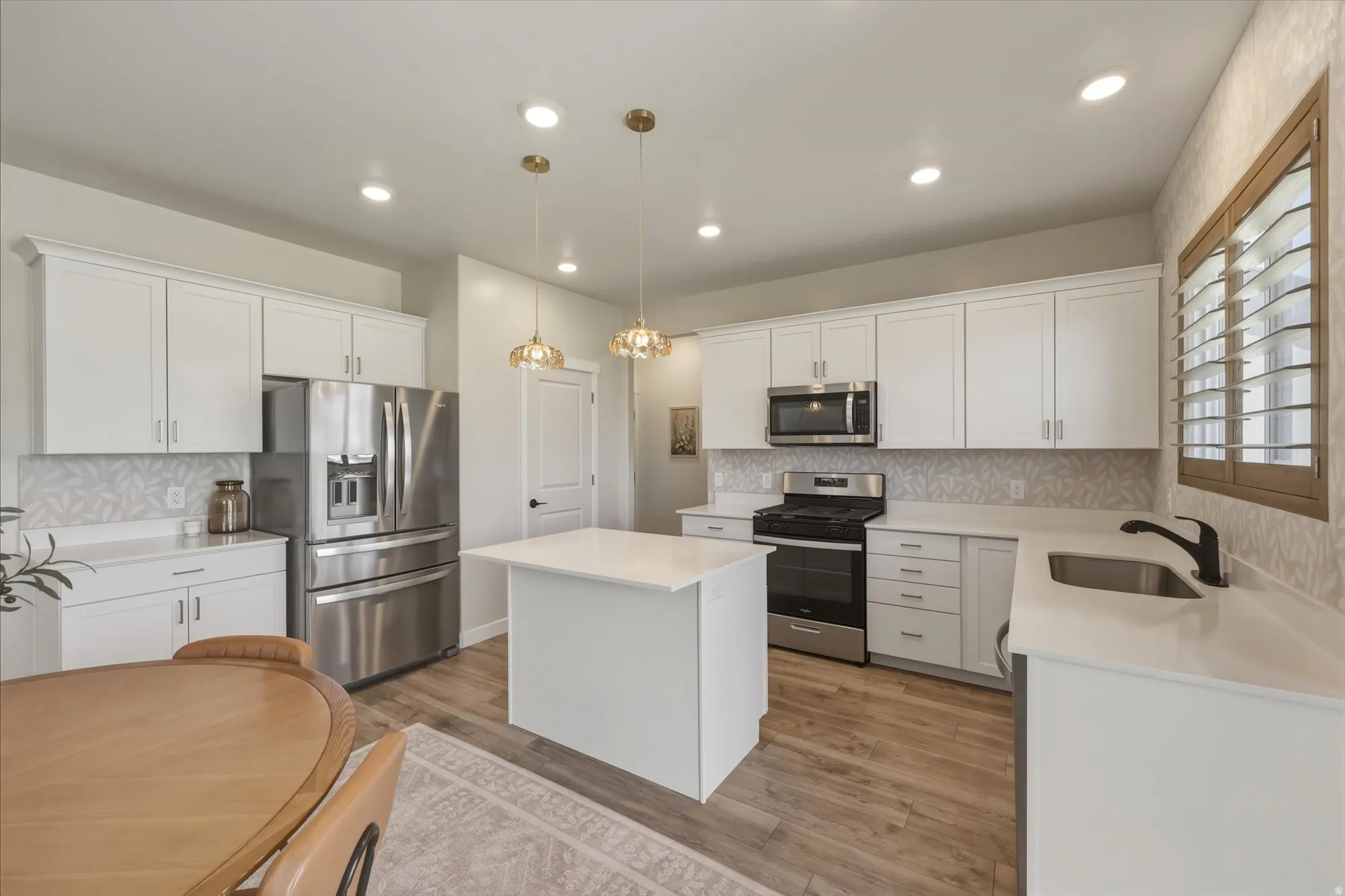 Modern kitchen featuring white cabinetry, stainless steel appliances, a center island with countertop seating, wood-finish flooring, and a decorative tile backsplash