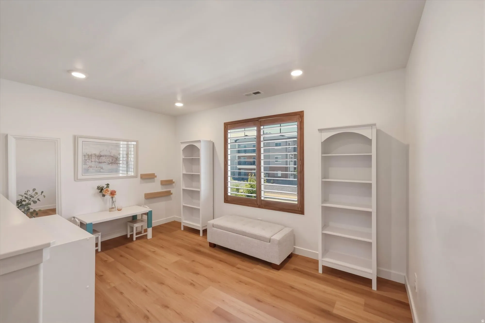 Spacious interior room featuring light wood-finish flooring, recessed lighting, and a window with plantation shutters and a wood-stained frame