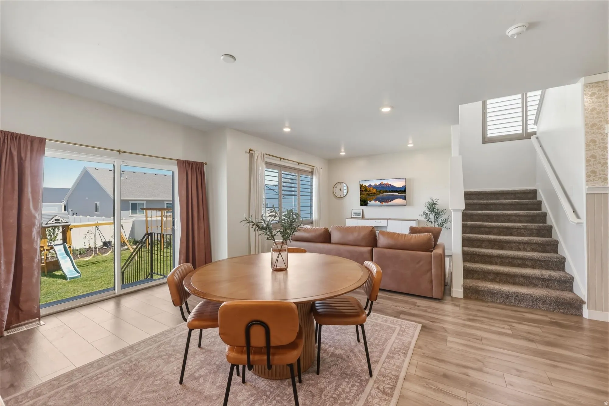 Open concept living space featuring wood-finish flooring, recessed lighting, a sliding glass patio door, and a carpeted staircase with white balusters