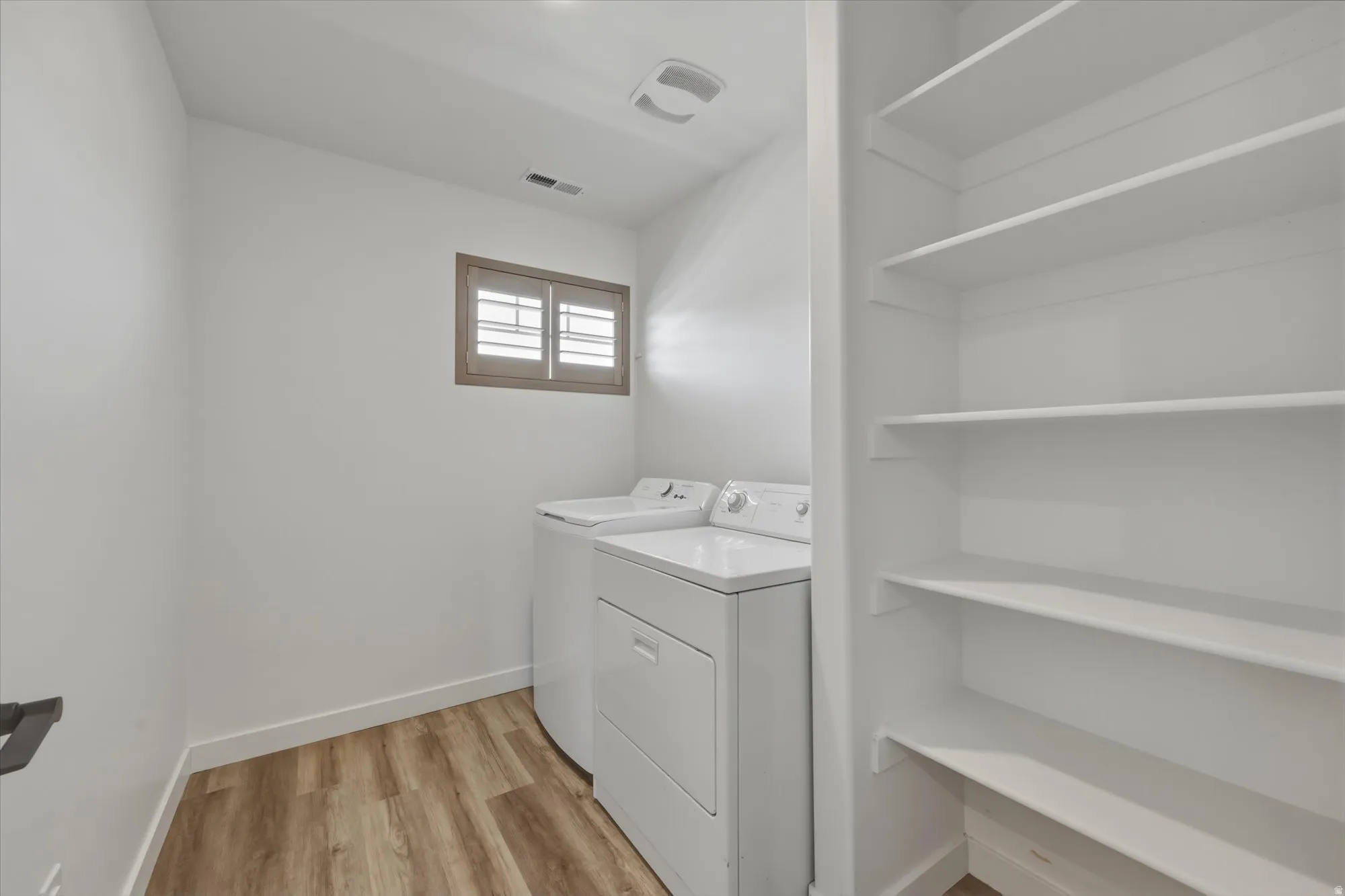 Dedicated laundry area featuring wood-finish flooring, a window with interior wooden shutters, overhead lighting, and built-in shelving