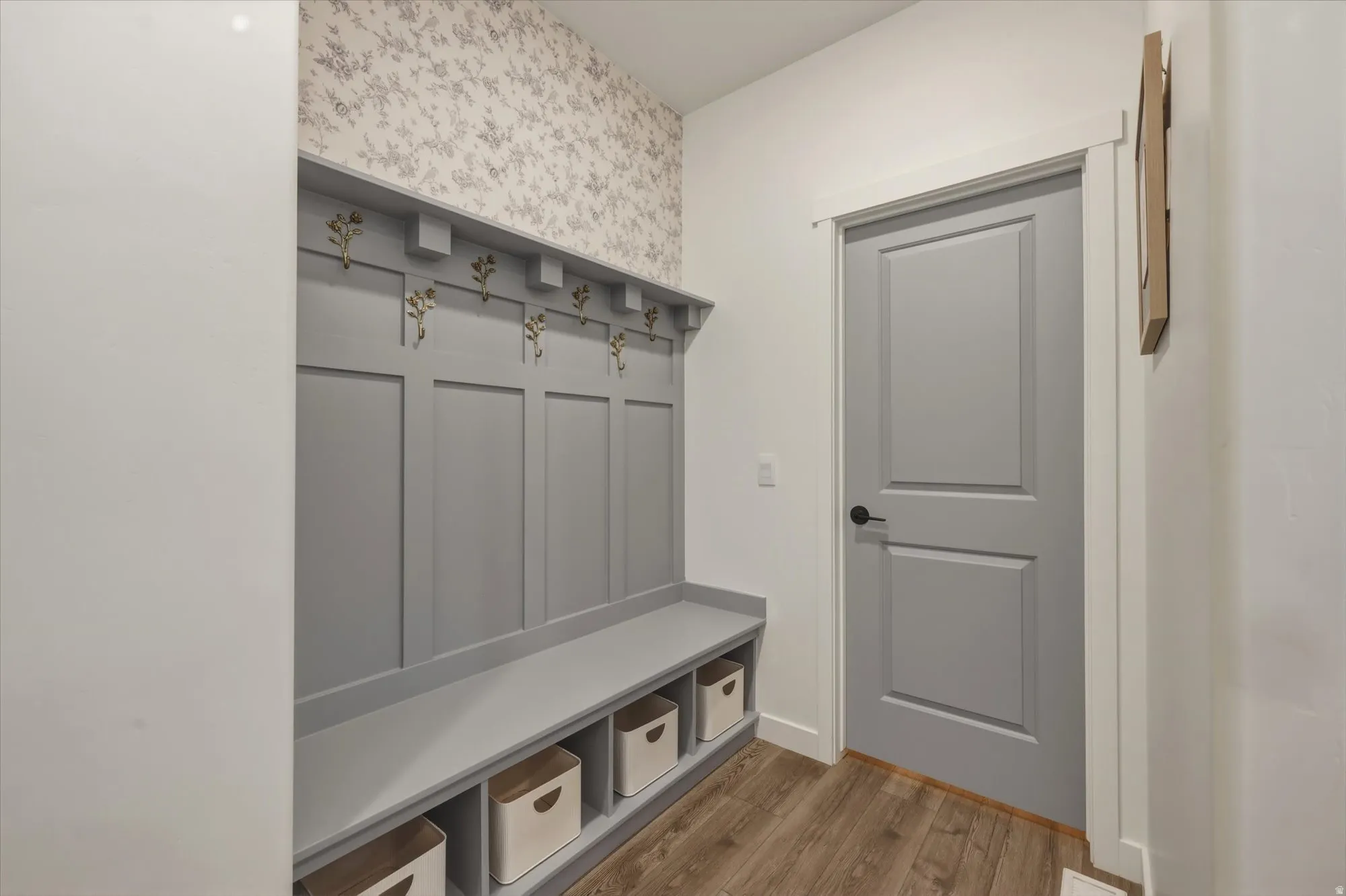 Built-in entryway storage bench with paneled wainscoting and decorative hooks, complemented by patterned wallpaper