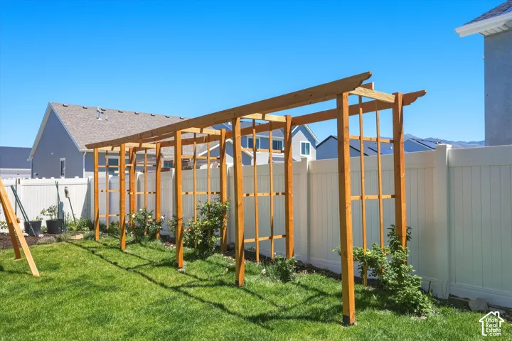 Expansive backyard featuring a wood trellis structure, manicured lawn, white privacy fencing, and garden beds