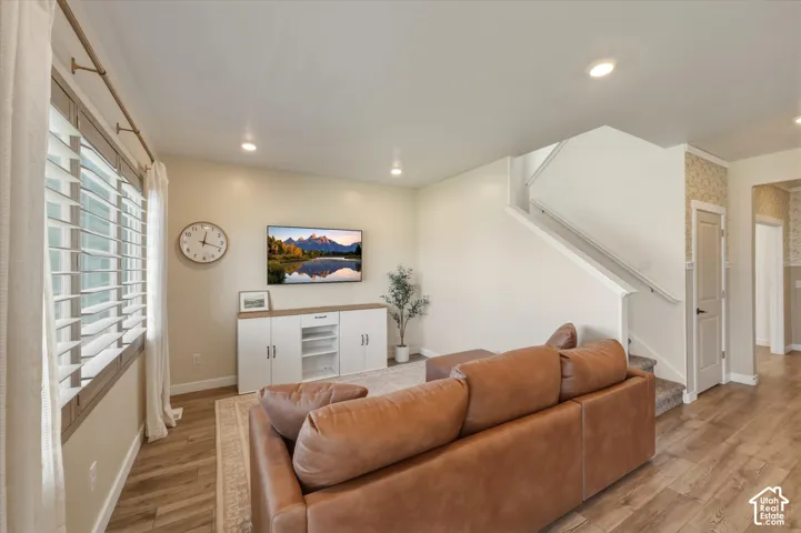 Living area featuring wood-finish flooring, recessed lighting, white window shutters, a staircase with white balusters, and a built-in media console with white cabinetry