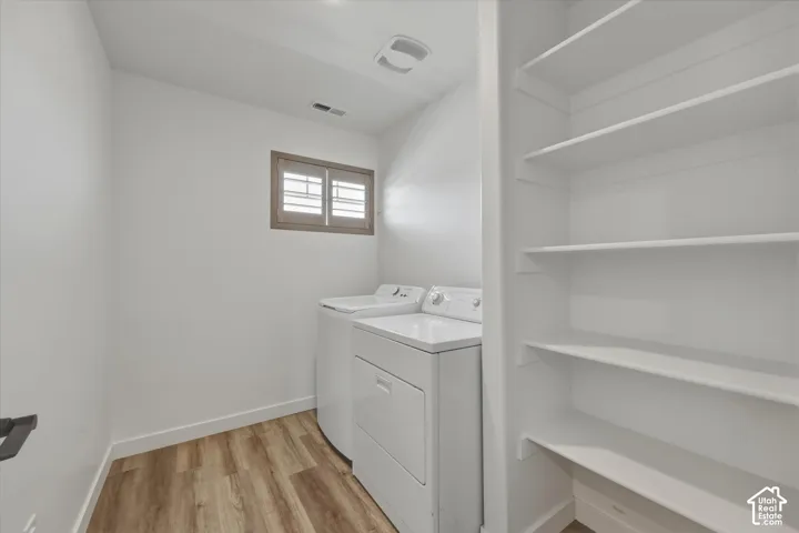 Dedicated laundry area featuring wood-finish flooring, a window with interior wooden shutters, overhead lighting, and built-in shelving