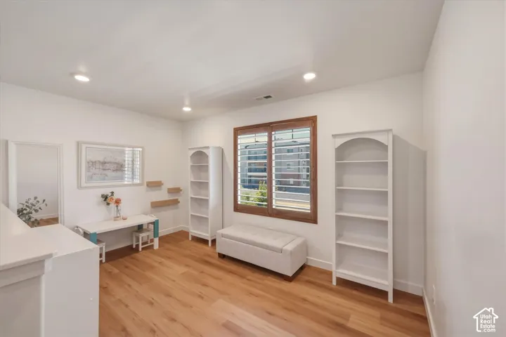 Spacious interior room featuring light wood-finish flooring, recessed lighting, and a window with plantation shutters and a wood-stained frame