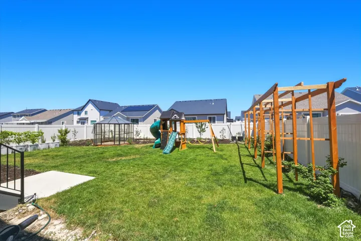 Expansive green lawn backyard featuring a white vinyl fence, a clear glass greenhouse structure, a natural wood arbor, and raised planter boxes