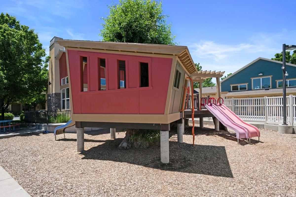 Outdoor play structure featuring a treehouse design with red and beige siding, two slides, and a wood chip ground cover