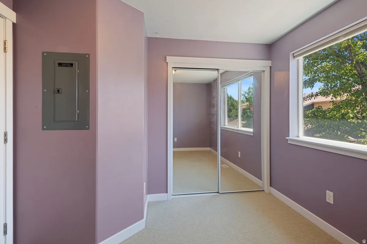 Carpeted room with lavender walls featuring a mirrored closet, a window with exterior tree foliage, and white trim throughout