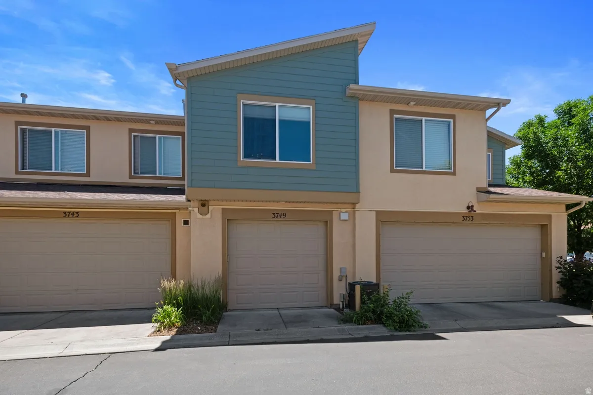 Townhome exterior featuring tan stucco and blue siding, attached garages, and individual entryways