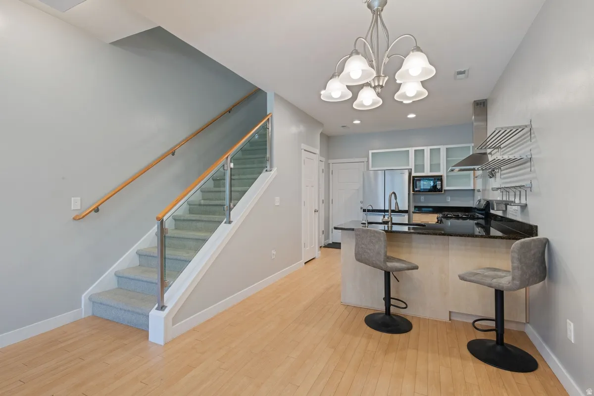 Open-concept interior featuring light wood-finish flooring, a contemporary kitchen, and a carpeted staircase with glass panel railing
