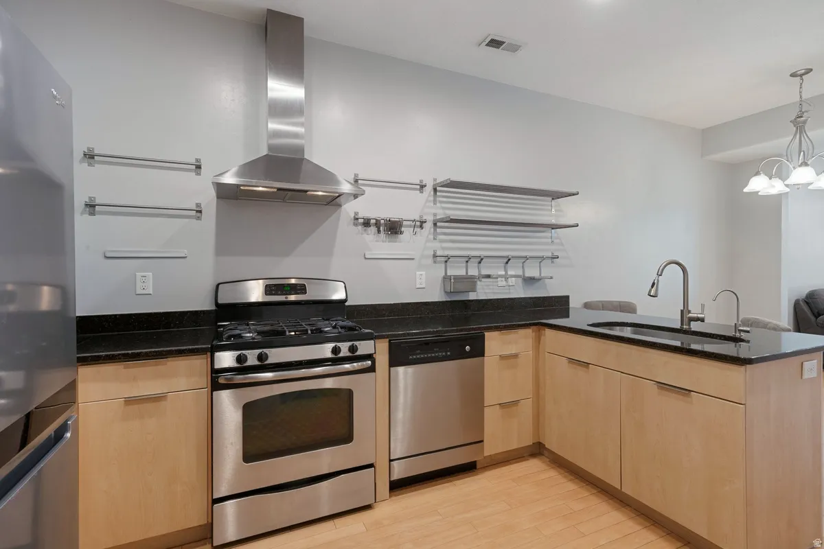 Contemporary kitchen featuring stainless steel appliances, light wood-finish cabinetry, black countertops, and a modern sink with a gooseneck faucet