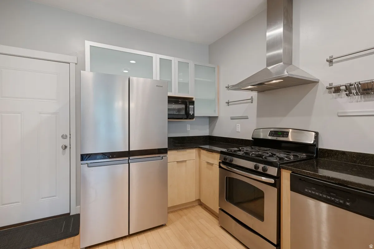 Kitchen featuring stainless steel appliances, dark stone countertops, light wood-finish cabinetry, a gas range with an overhead vent hood, and a built-in microwave