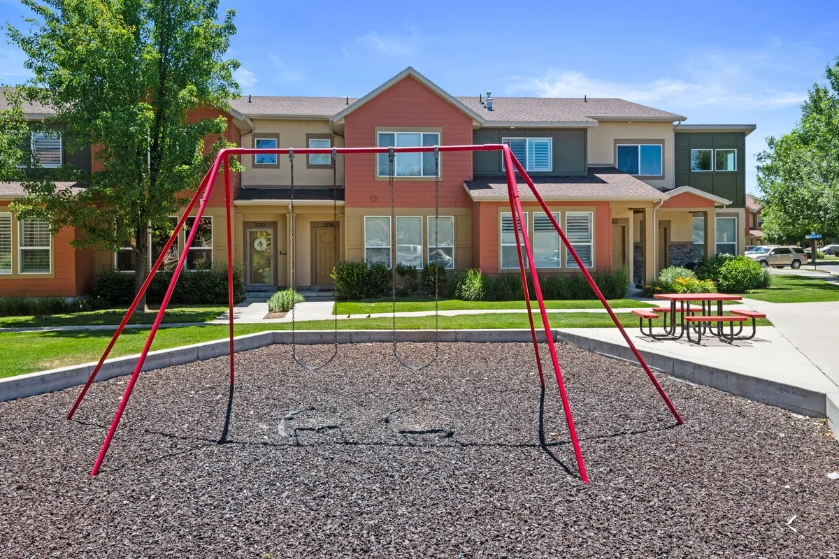 Community park area featuring a swing set with safety surfacing, a picnic table, and concrete pathways