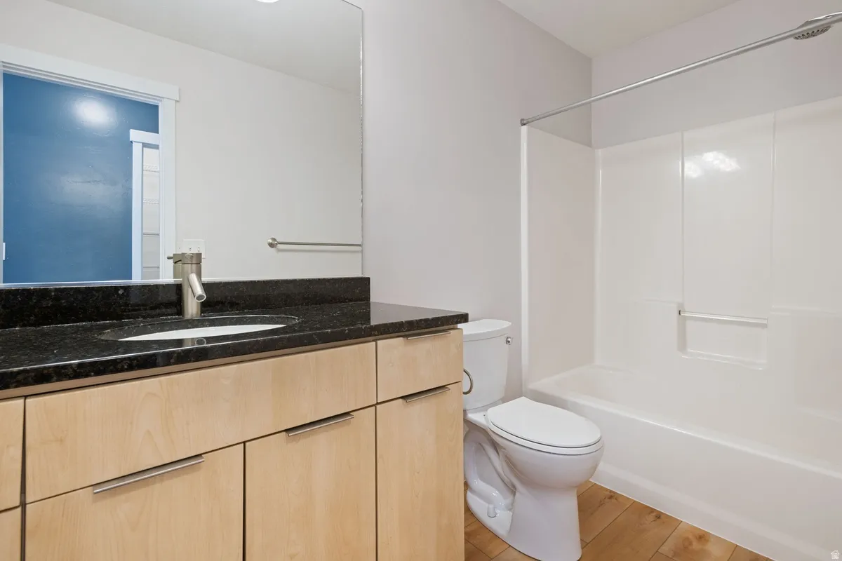 Bathroom featuring a neutral color palette, wood-finish flooring, a light-toned wood vanity with brushed nickel hardware, a black countertop, and an integrated white sink