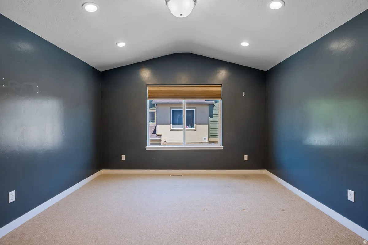 Carpeted room with a vaulted ceiling, recessed lighting, and a central window with blinds